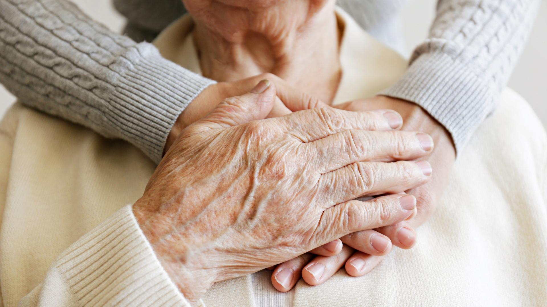 Eine Frau umarmt eine ältere Frau und hält ihre Hände.