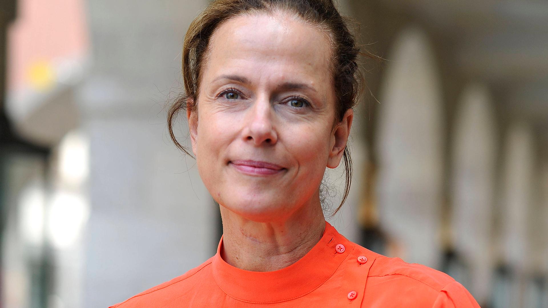 Claudia Michelsen lächelt in die Kamera. Sie trägt eine orange Bluse und das braune Haar aufgesteckt.