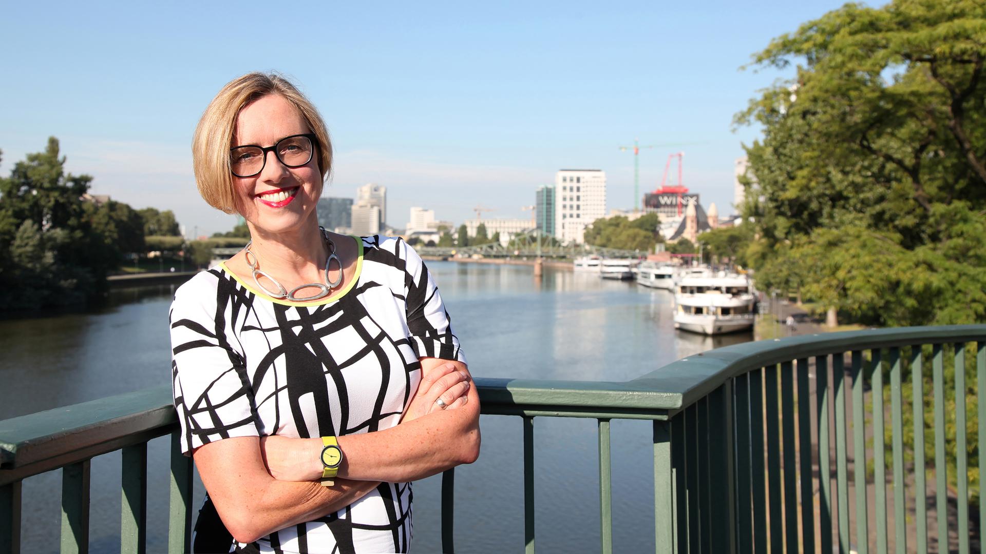 Ursula Ott steht in einem schwarzweißen Kleid auf einer Brücke über den Main