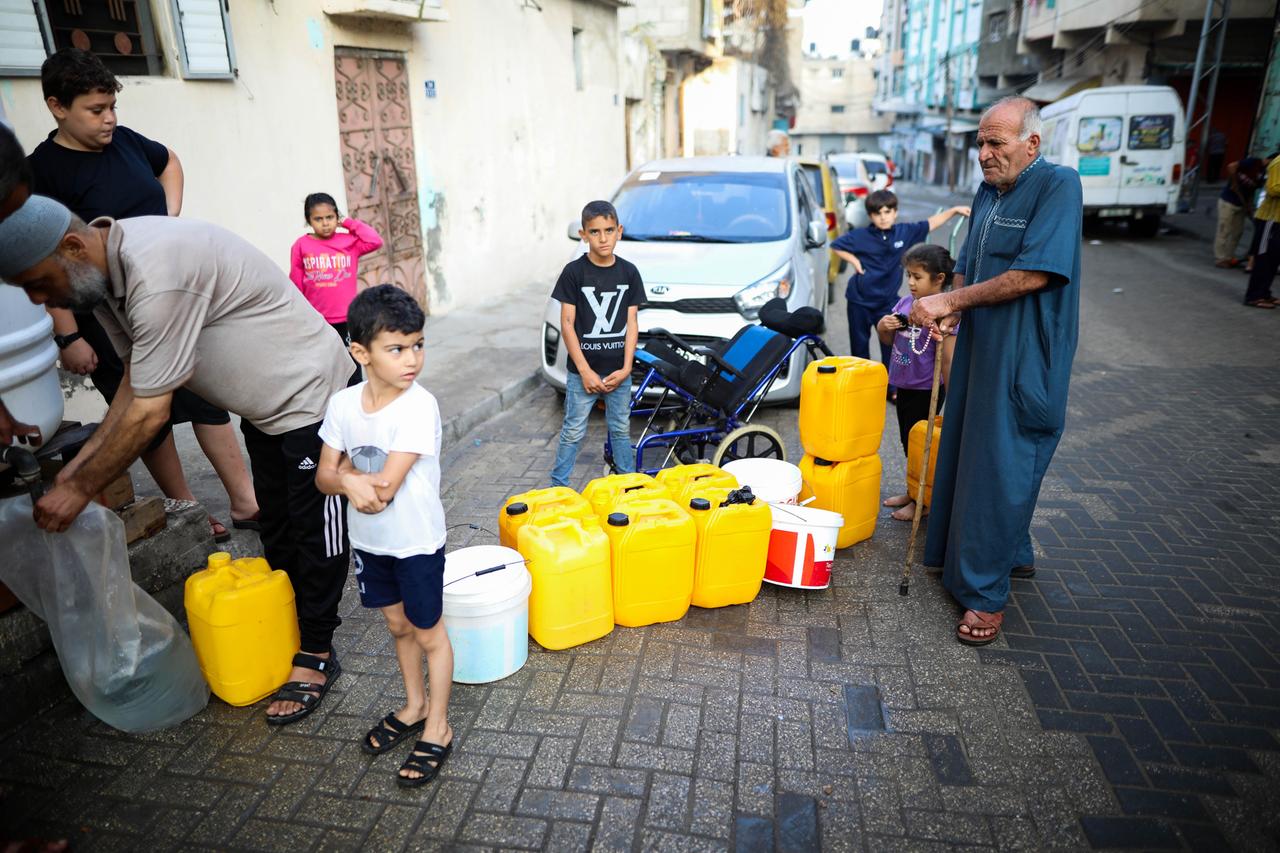 Palästinenser im Gazastreifen stehen Schlange, um sich mit Trinkwasser aus einem Tank zu versorgen. Zu sehen sind mehrere Kinder und zwei alte Männer, die Kanister dabei haben.