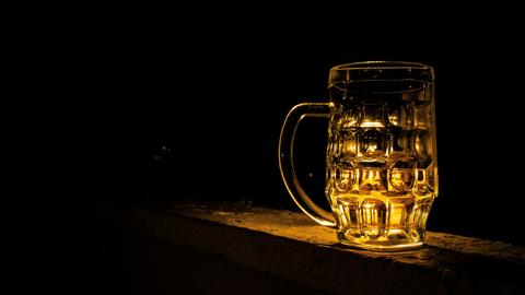Ein leerer Bierkrug aus Glas vor einem schwarzen Hintergrund wird golden angeleuchtet.
