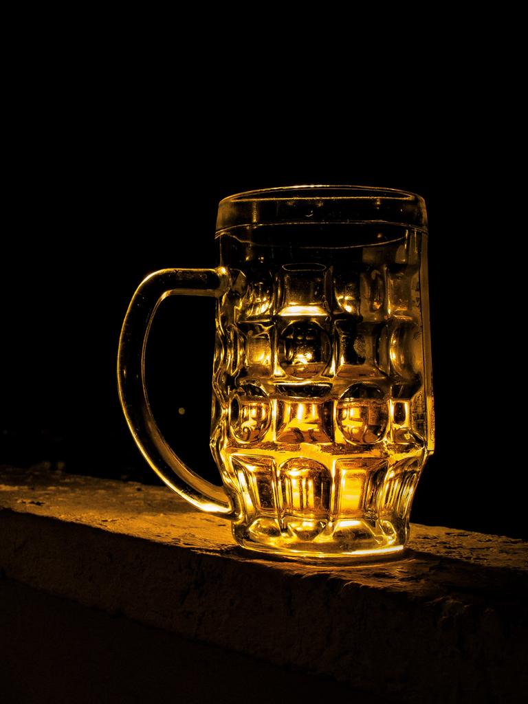 Ein leerer Bierkrug aus Glas vor einem schwarzen Hintergrund wird golden angeleuchtet.