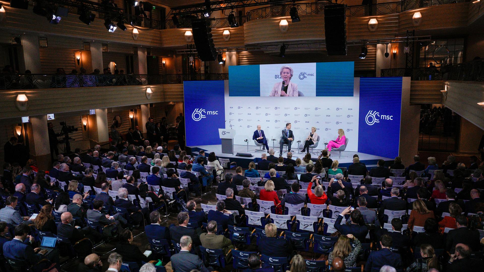 Das Bild zeigt Zuschauer von hinten in einem großen Saal der Münchner Sicherheitskonferenz. Vorn ist ein Podium zu erkennen, dort spricht EU-Kommissionspräsidentin von der Leyen in ein Mikrofon.