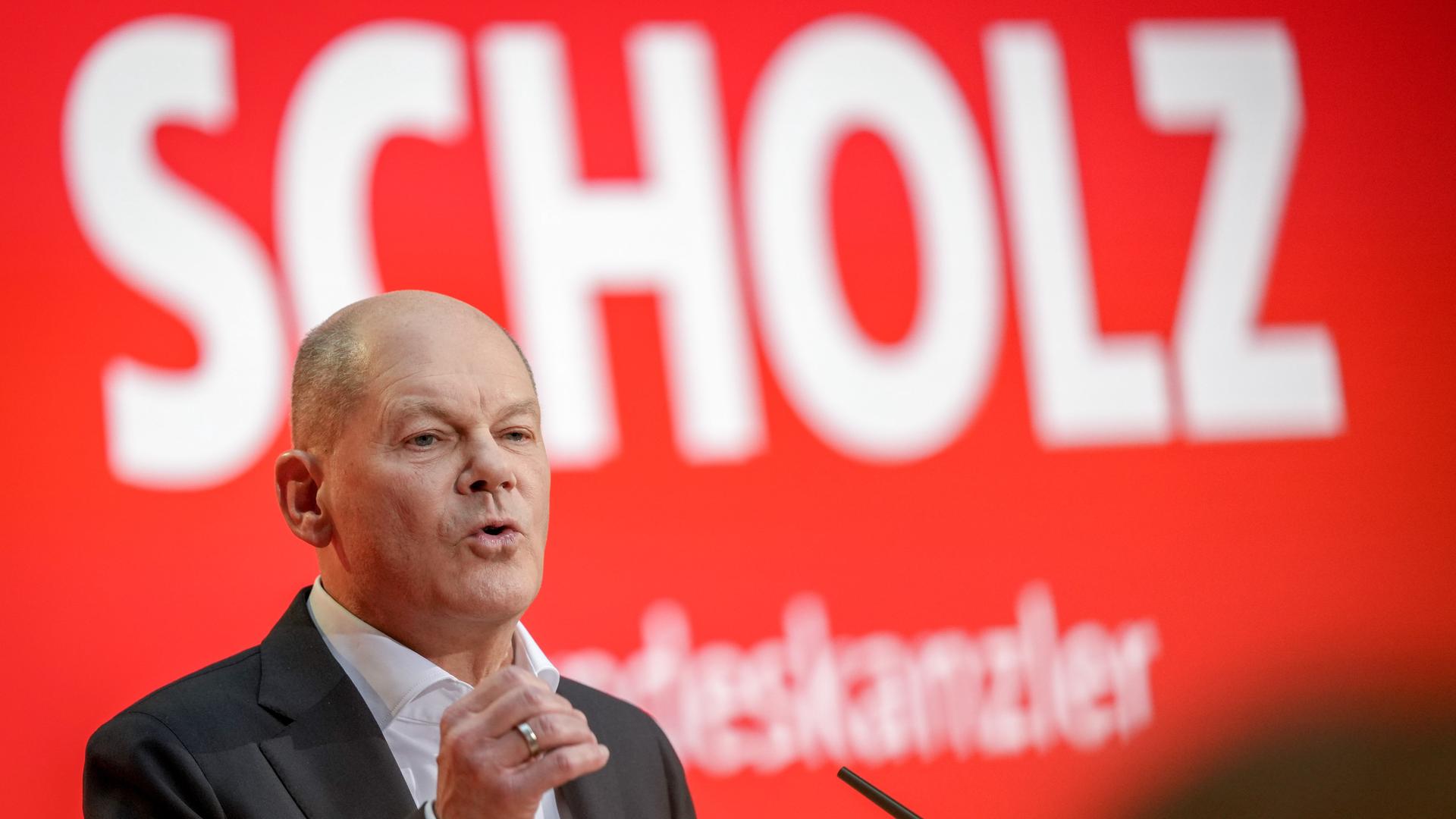 Olaf Scholz hält seine Rede vor einem roten Hintergrund. Darauf zu lesen stehen in großen, weißen Buchstaben die Worte "Scholz" und "Bundeskanzler".