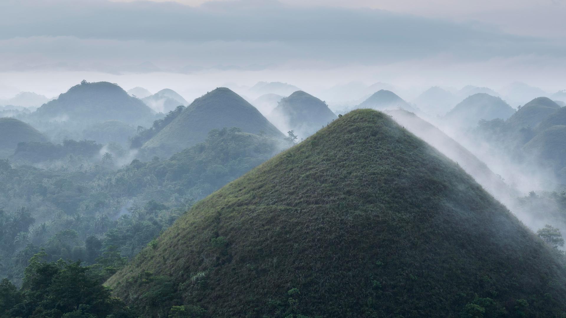 Panoramablick auf die Chocolate Hills auf der Insel Bohol auf den Philippinen bei Sonnenaufgang mit Dunst und Nebel. Panoramablick auf die Chocolate Hills auf der Insel Bohol auf den Philippinen bei Sonnenaufgang mit Dunst und Nebel.