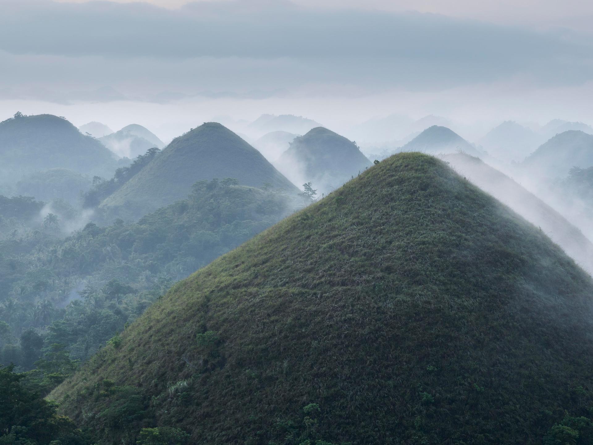 Panoramablick auf die Chocolate Hills auf der Insel Bohol auf den Philippinen bei Sonnenaufgang mit Dunst und Nebel.