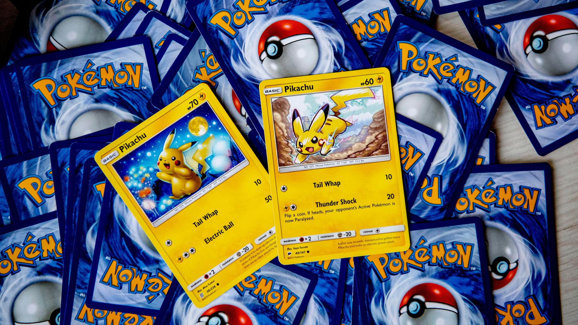 Pokemon-Karten liegen mit der Rückseite nach oben verstreut auf einem Tisch. Zwei Karten mit Pikachu darauf sein richtig herum zu sehen. 
