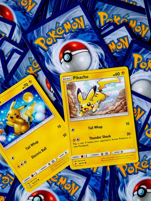 Pokemon-Karten liegen mit der Rückseite nach oben verstreut auf einem Tisch. Zwei Karten mit Pikachu darauf sein richtig herum zu sehen. Pokemon-Karten liegen mit der Rückseite nach oben verstreut auf einem Tisch. Zwei Karten mit Pikachu darauf sein richtig herum zu sehen.