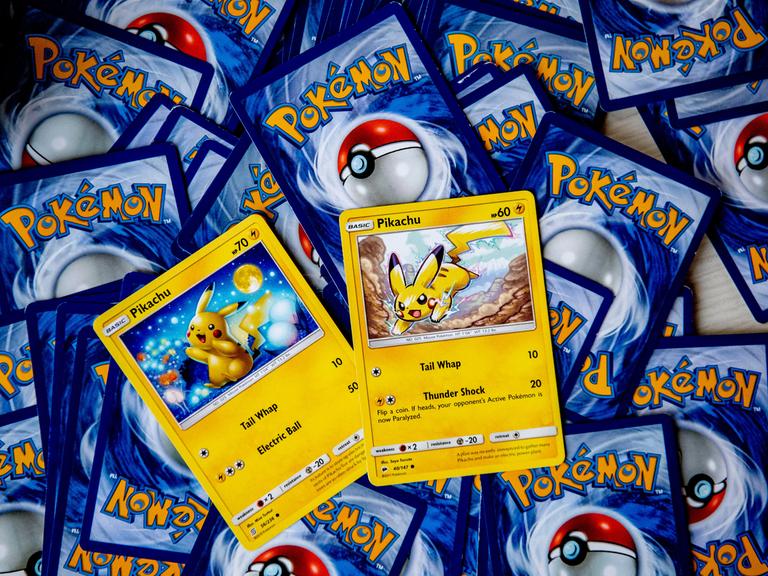Pokemon-Karten liegen mit der Rückseite nach oben verstreut auf einem Tisch. Zwei Karten mit Pikachu darauf sein richtig herum zu sehen. Pokemon-Karten liegen mit der Rückseite nach oben verstreut auf einem Tisch. Zwei Karten mit Pikachu darauf sein richtig herum zu sehen.