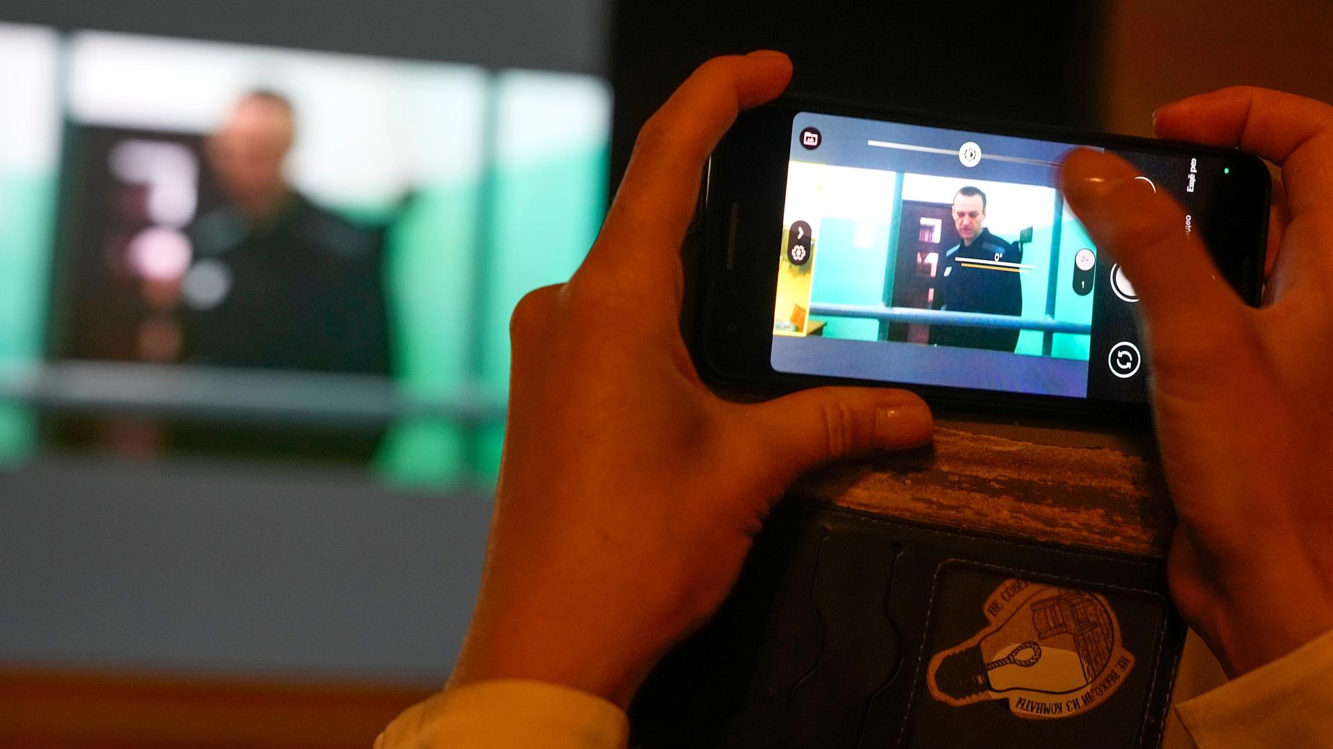 Ein Journalist macht mit dem Smartphone ein Foto vom Bildschirm, auf dem Alexei Nawalny während einer Anhörung zu sehen ist.