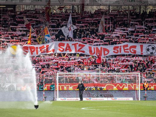 Fans von Union Berlin halten ein Banner mit der Aufschrift "Spiel, Satz und Sieg" in der Fankurve hoch.