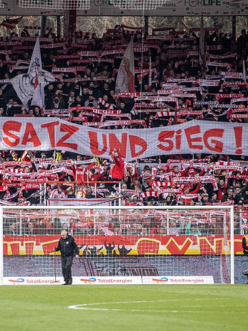 Fans von Union Berlin halten ein Banner mit der Aufschrift "Spiel, Satz und Sieg" in der Fankurve hoch.