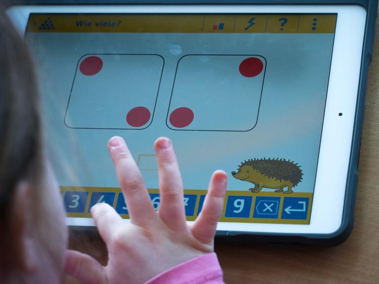 Kinderfinger tippen auf einem Tablet auf dem spielerisch eine Rechenaufgabe dargestellt ist.