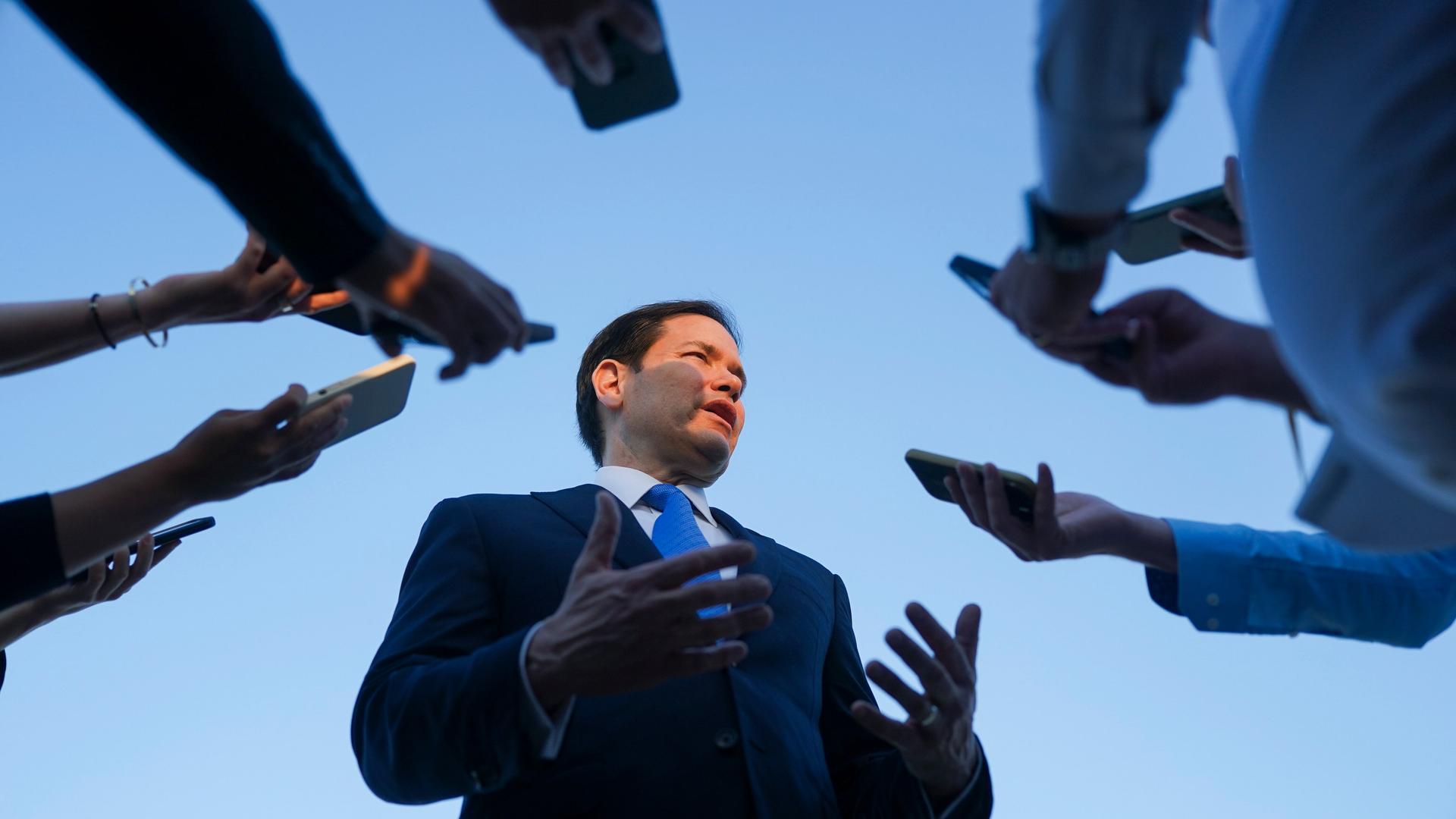 US-Außenminister Rubio vor seinem Abflug nach Katar, er ist umgeben von Journalisten, die ihm ihre Aufnahmegeräte hinhalten. 