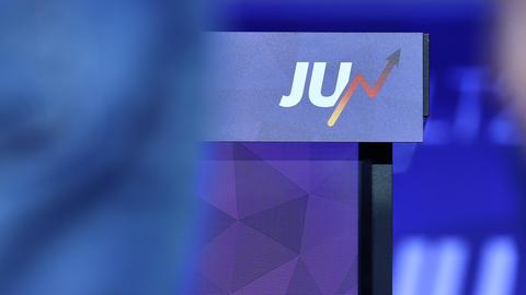 Das Foto zeigt in der Mitte ein Rednerpult. Daran hängt das Logo der Jungen Union: die Großbuchstaben „JU“ in weißer Schrift vor blauem Grund. 