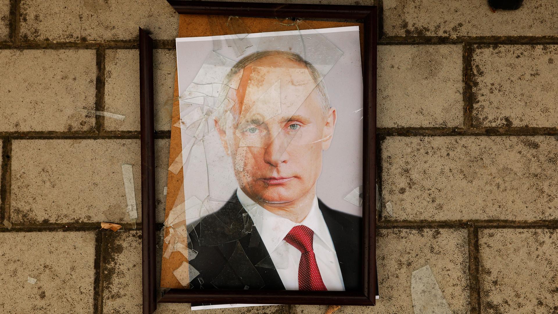 Auf dem Fußboden liegt ein gerahmtes Porträt von Wladimir Putin mit zerbrochenem Deckglas.