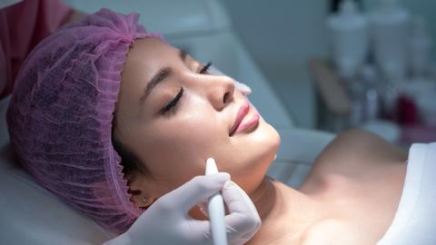 Eine Frau liegt für eine kosmetische Behandlung auf einer Liege. Sie trägt ein rosafarbenes Haarnetz. Eine Frau liegt für eine kosmetische Behandlung auf einer Liege. Sie trägt ein rosafarbenes Haarnetz.