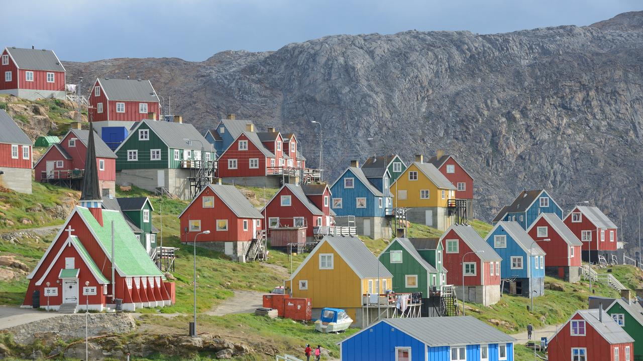 Der Ort Upernavik in Grönland. Bunte Häuser stehen in einer wunderschönen Naturlandschaft. Um die Häuser wächst grünes Grass. Im Hintergrund ein Fels.