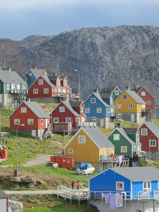 Der Ort Upernavik in Grönland. Bunte Häuser stehen in einer wunderschönen Naturlandschaft. Um die Häuser wächst grünes Grass. Im Hintergrund ein Fels.