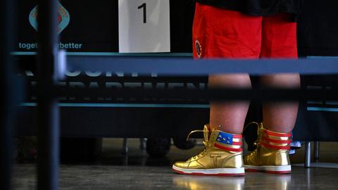 Ein Mann trägt goldene Sneaker mit amerikanischer Flagge und einem "T" für Trump.