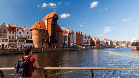 Weibliche Reisende mit Rucksack bewundert historische Uferpromenade und mittelalterlichen Kran in Danzig.