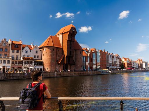 Weibliche Reisende mit Rucksack bewundert historische Uferpromenade und mittelalterlichen Kran in Danzig.