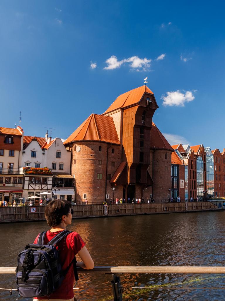 Weibliche Reisende mit Rucksack bewundert historische Uferpromenade und mittelalterlichen Kran in Danzig.
