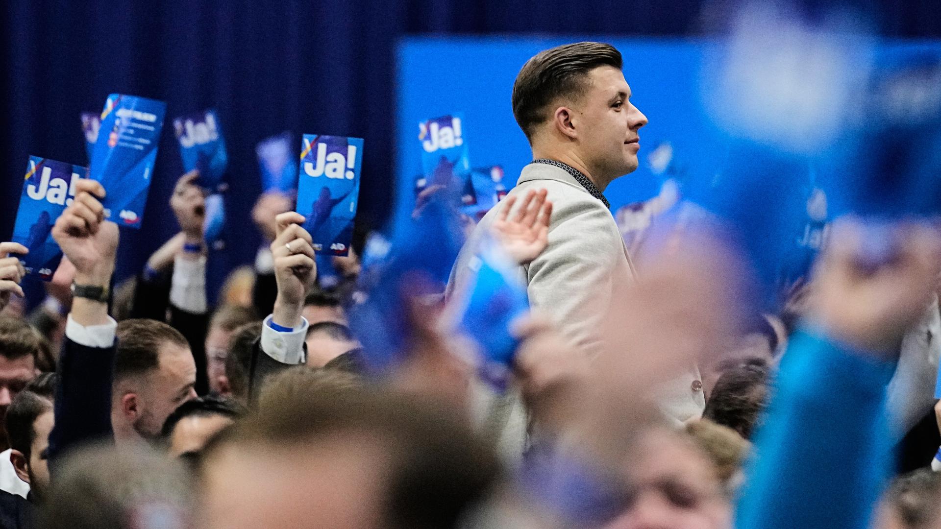 Jean-Pascal Hohm ist im Profil zu sehen, wie er zwischen anderen Parteimitgliedern steht, die Karten mit der Aufschrift "JA!" in die Luft strecken.