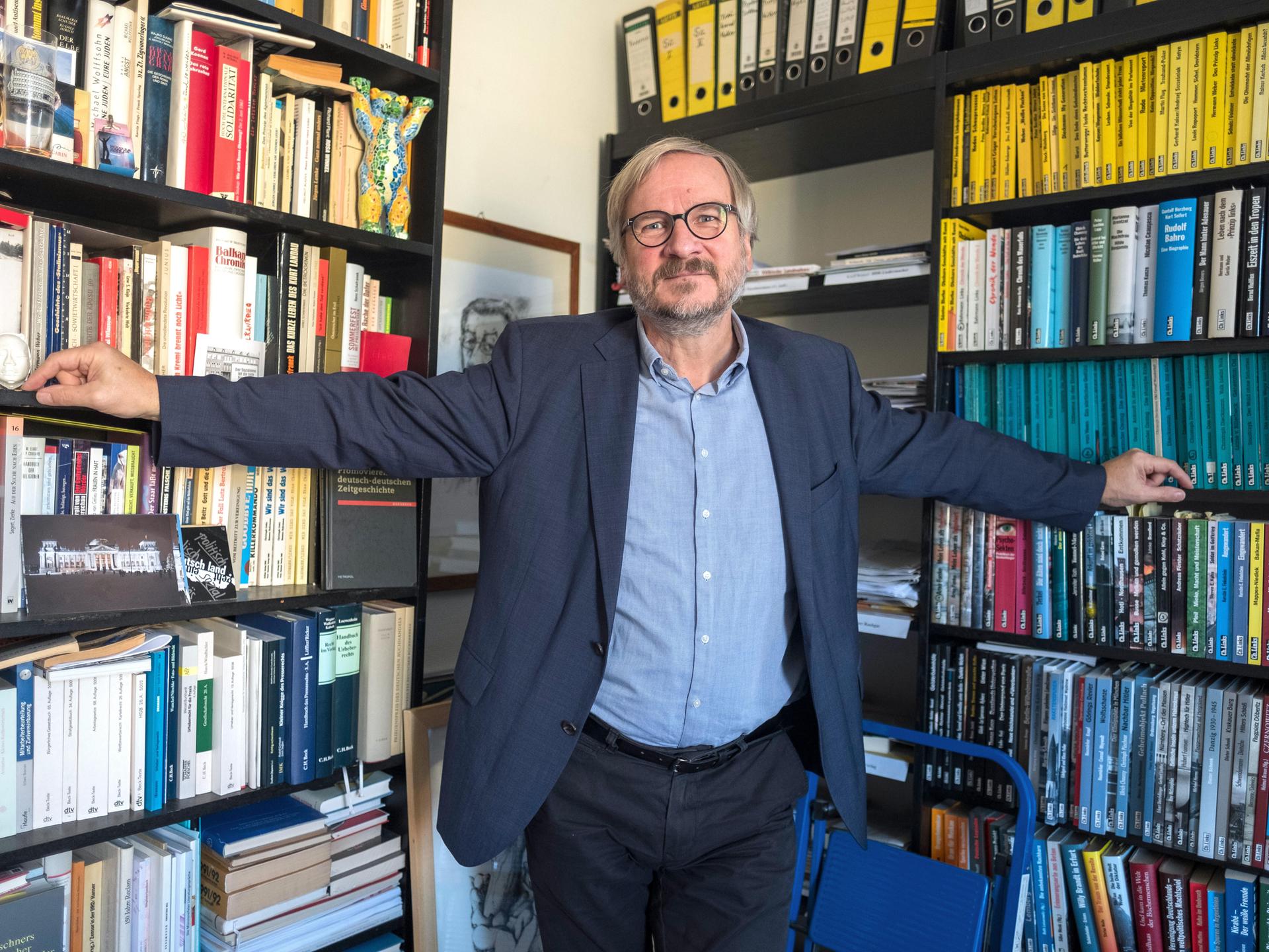 Verleger Christoph Links steht mit ausgebreiteten Armen vor vollen Bücherregalen in seinem Verlag in Berlin.