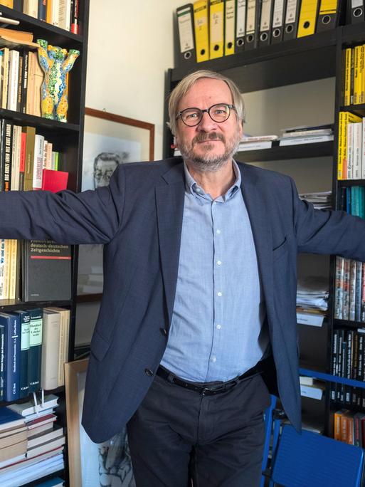 Verleger Christoph Links steht mit ausgebreiteten Armen vor vollen Bücherregalen in seinem Verlag in Berlin.