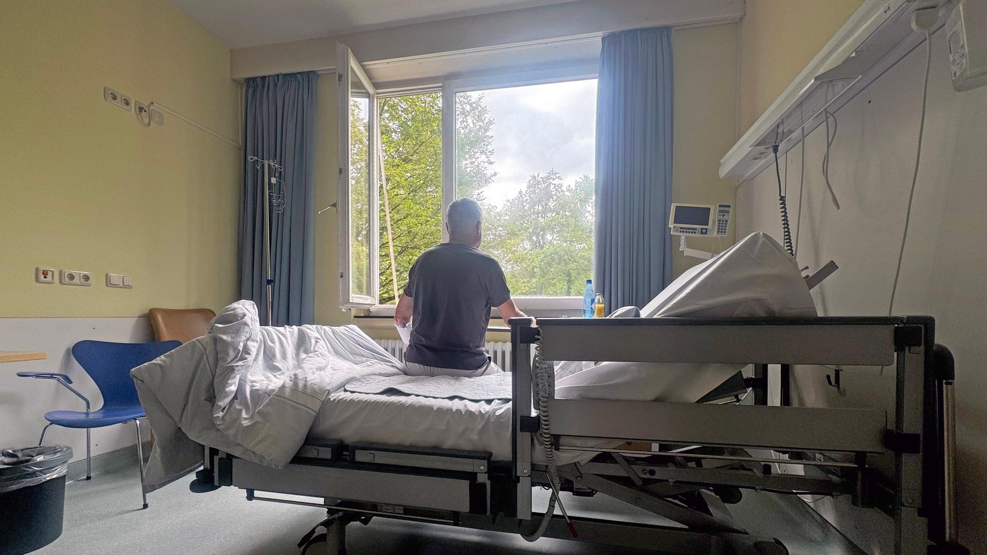 Ein Patient sitzt im Krankenhaus in seinem Einzelzimmer auf dem Bett.