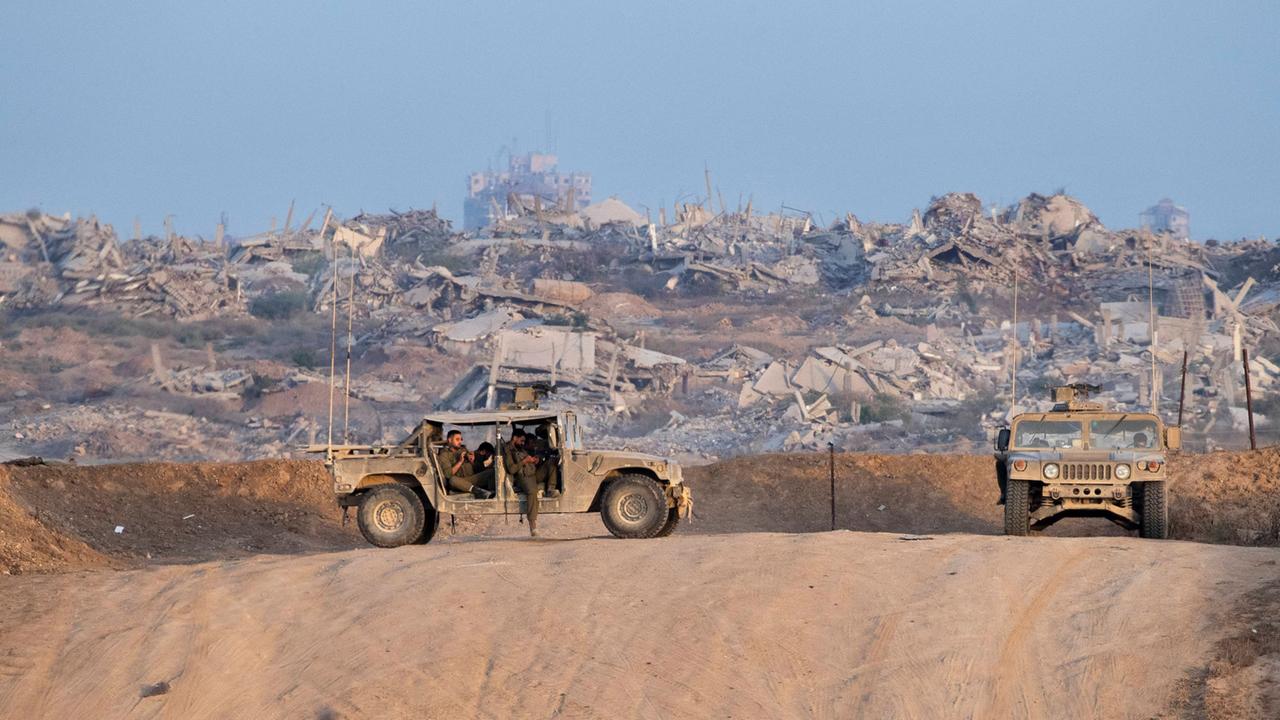Israelische Soldaten stehen mit zwei Geländewägen an der Grenze zu Gaza. Im Hintergrund sieht man zersörte Häuser. Israelische Soldaten stehen mit zwei Geländewägen an der Grenze zu Gaza. Im Hintergrund sieht man zersörte Häuser.
