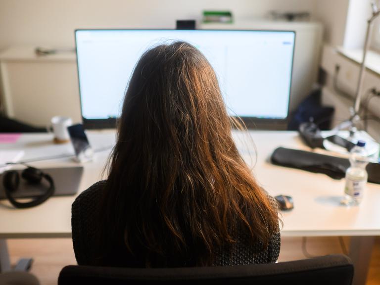 Ein Frau sitzt an einem Arbeitsplatz vor einem Computer (gestellte Szene).