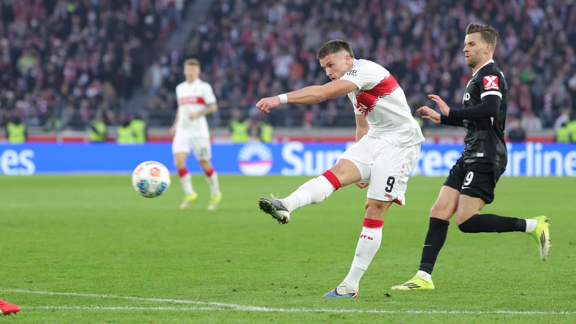Ein Fußballer im weißen Trikot schießt mit dem Ball auf das Tor.
