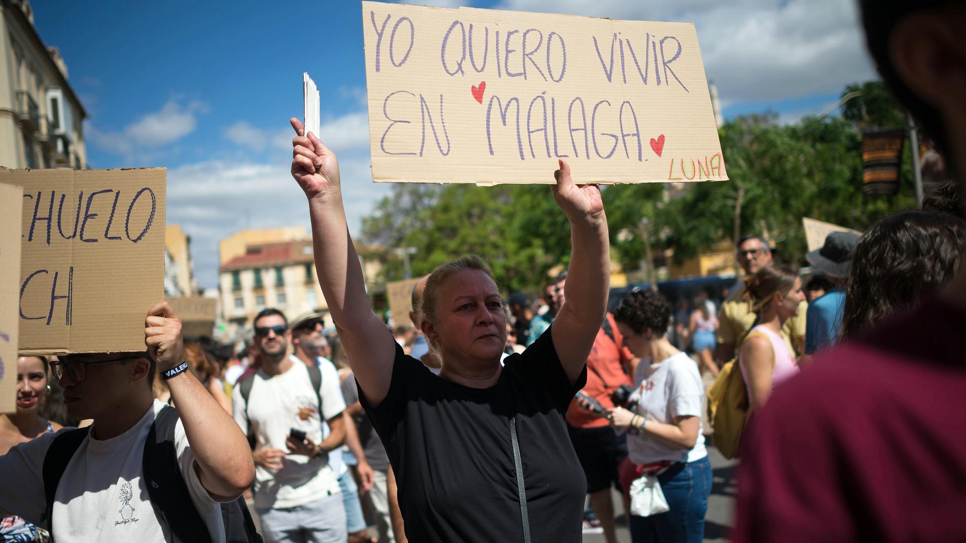 Eine Demonstrantin hält in einer Gruppe von Menschen ein Schild hoch, um gegen den Massentourismus in Malaga zu protestieren.