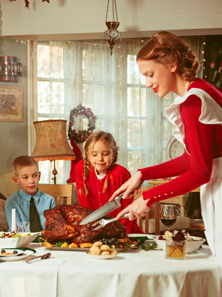 Familie bei einem Festmahl. Eine Frau im Look der 50er-Jahre schneidet einen prächtigen Braten an, auf den Mann und zwei Kinder freudig schauen.