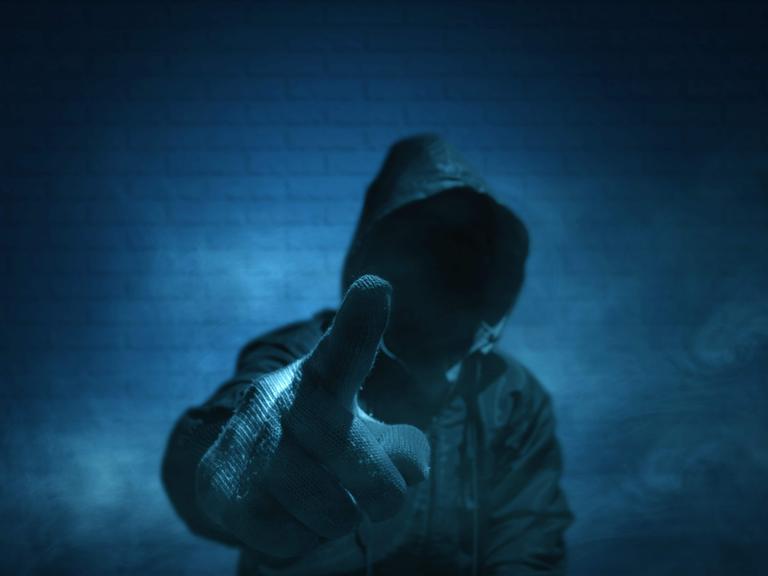 Ein unkenntlicher Mann mit Hoodie und erhobenem Zeigefinger in Handschuhen. Ein unkenntlicher Mann mit Hoodie und erhobenem Zeigefinger in Handschuhen.