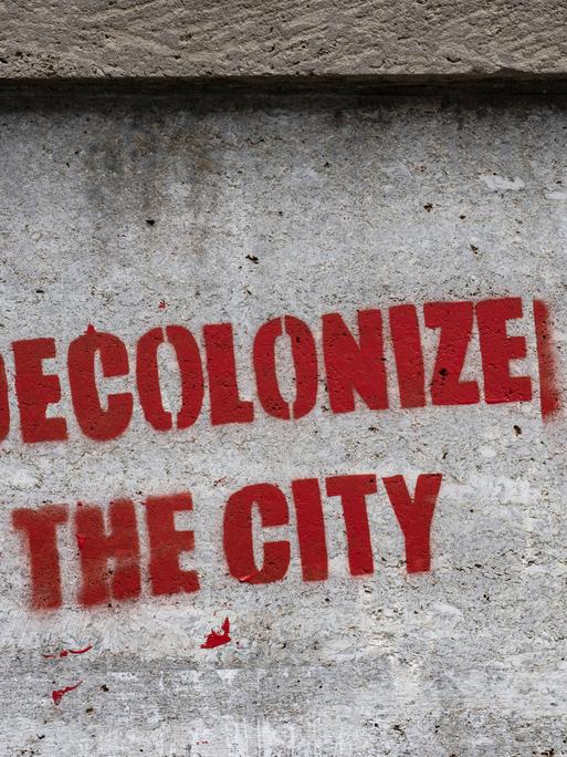 Ein Graffiti mit dem Schriftzug "decolonize the city" wurde an eine Botenpfeiler gesprüht.