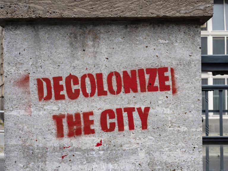 Ein Graffiti mit dem Schriftzug "decolonize the city" wurde an eine Botenpfeiler gesprüht.