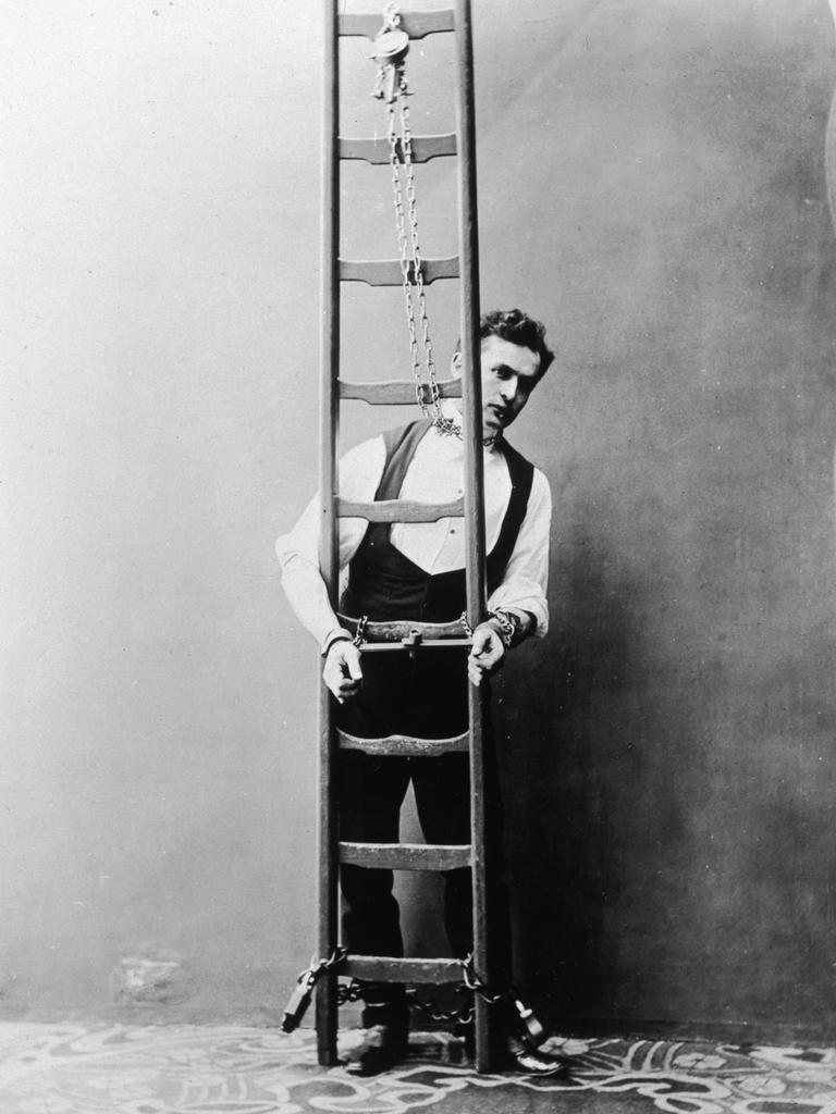 Historisches Schwarz-Weiß-Foto von Harry Houdini, der mit Ketten an Händen und Hals an eine Leiter gekettet ist.