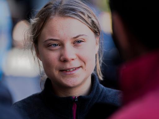 Die schwedische Klimaaktivistin Greta Thunberg schaut freundlich aber ernst eine Person an, mit der sie im Gespräch ist, und die mit dem Rücken zur Kamera steht.