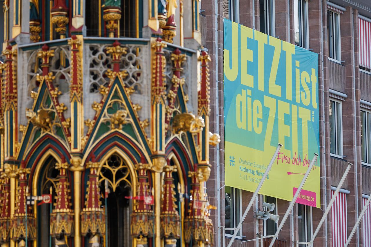 Ein Plakat zum Evangelischen Kirchentag mit dem Slogan "Jetzt ist die Zeit" hängt an der Außenfassade des Nürnberger Rathauses am Hauptmarkt. Im Vordergrund ist der "Schöne Brunnen" zu erkennen.