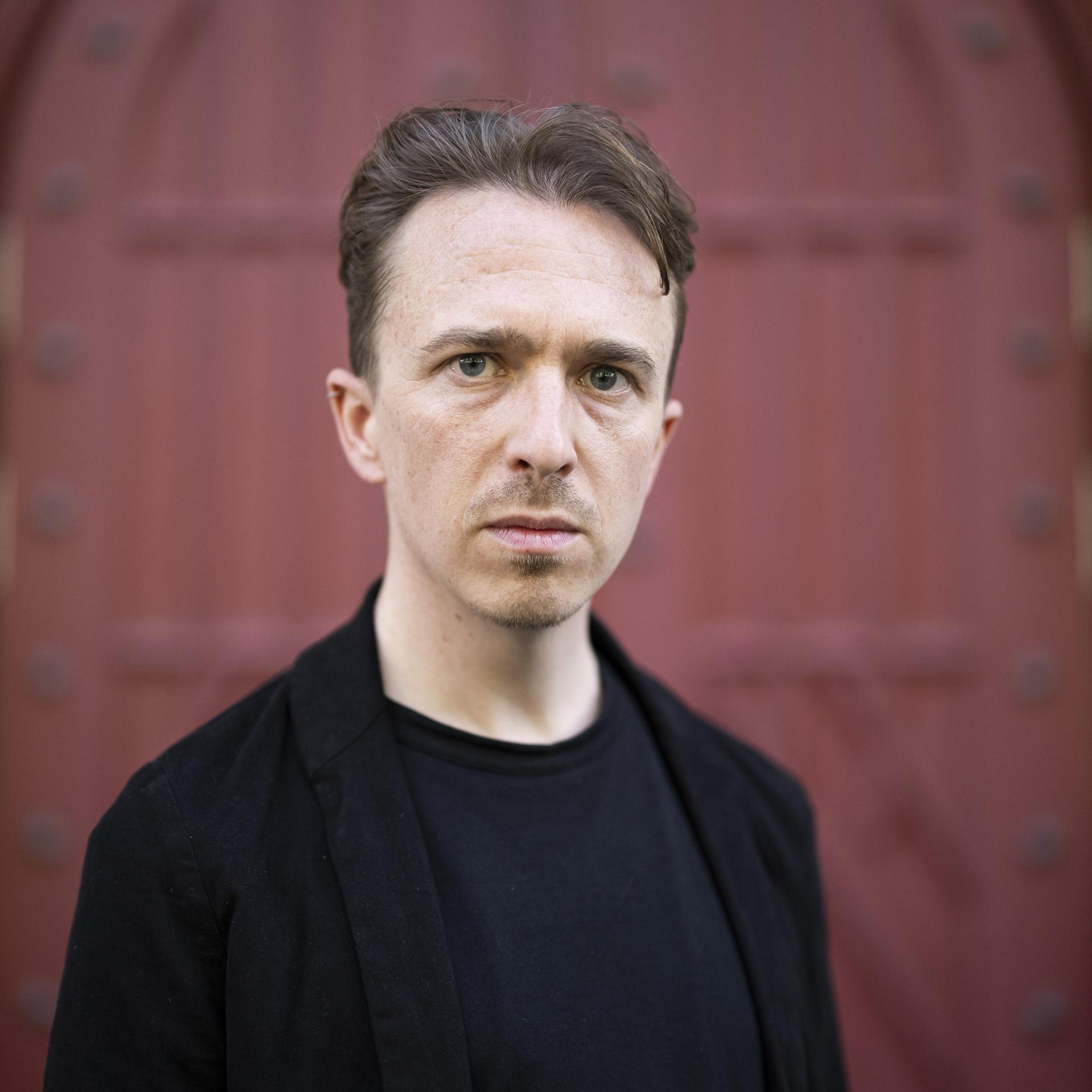 Der Schweizer Schriftsteller Béla Rothenbuehler posiert vor einem Tor.  