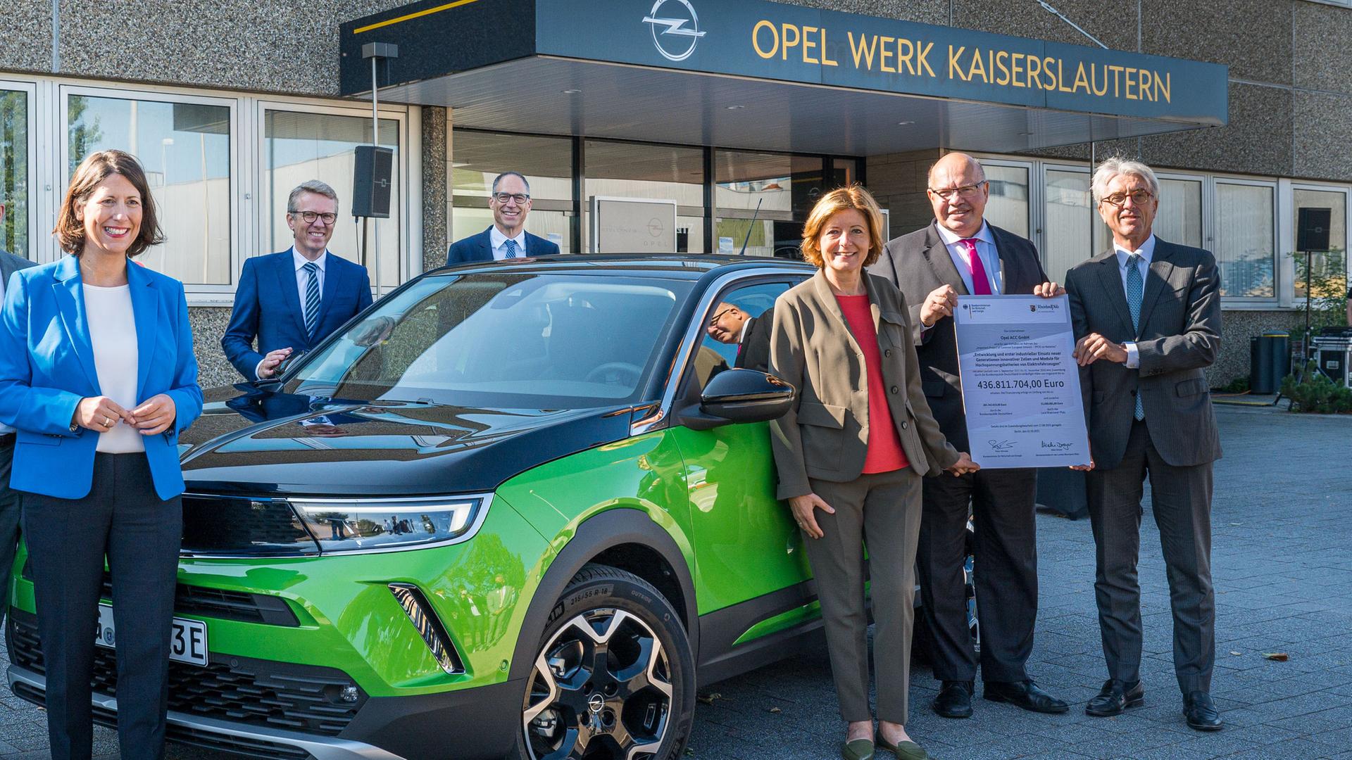 Die rheinland-pfälzische Ministerpräsidentin Malu Dreyer überreicht gemeinsam mit Bundeswirtschaftsminister Peter Altmaier einen Zuwendungsbescheid. Sie stehen vor einem Elektro-Auto. Im Hintergrund ist an einem Gebäude der Schriftzug "Opel Werk Kaiserslautern" zu sehen. Die rheinland-pfälzische Ministerpräsidentin Malu Dreyer überreicht gemeinsam mit Bundeswirtschaftsminister Peter Altmaier einen Zuwendungsbescheid. Sie stehen vor einem Elektro-Auto. Im Hintergrund ist an einem Gebäude der Schriftzug "Opel Werk Kaiserslautern" zu sehen.