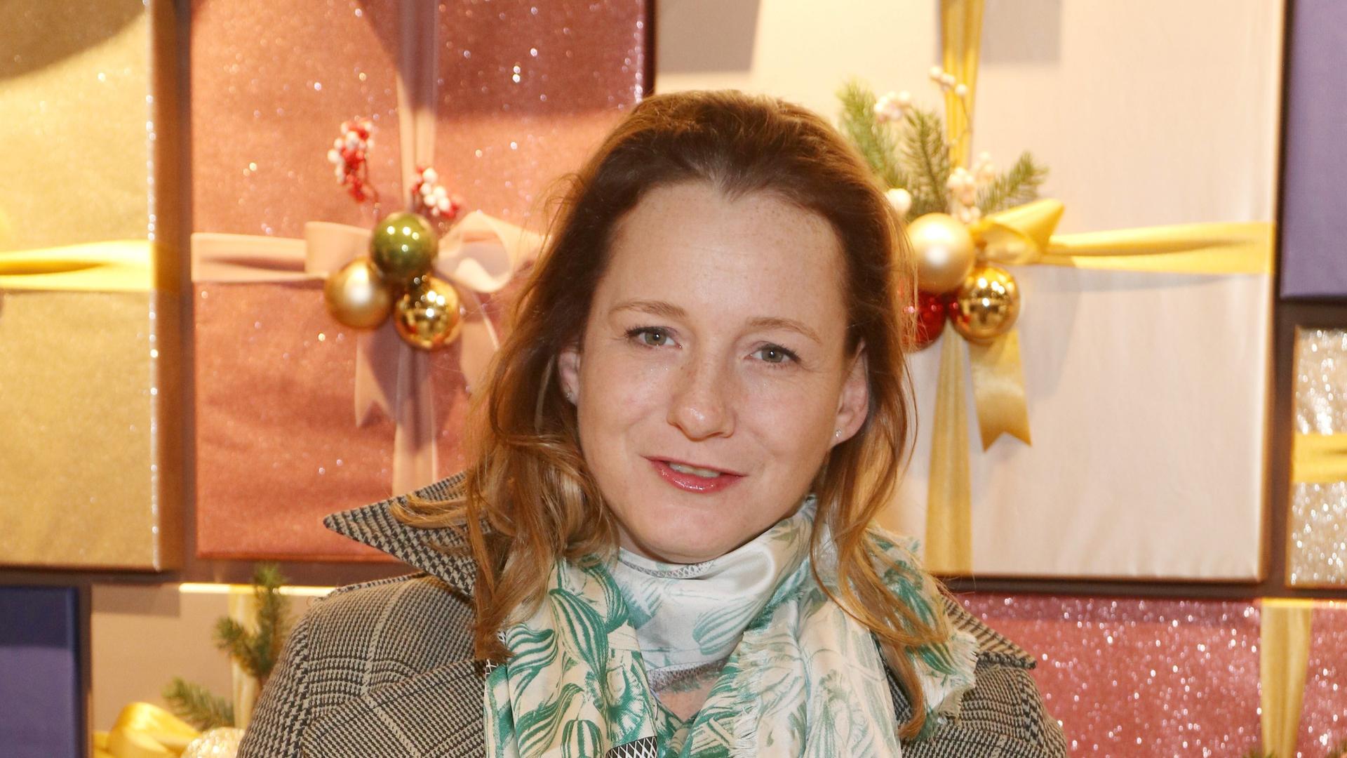 Jenny Falckenberg steht vor verpackten Geschenken und lächelt in die Kamera.