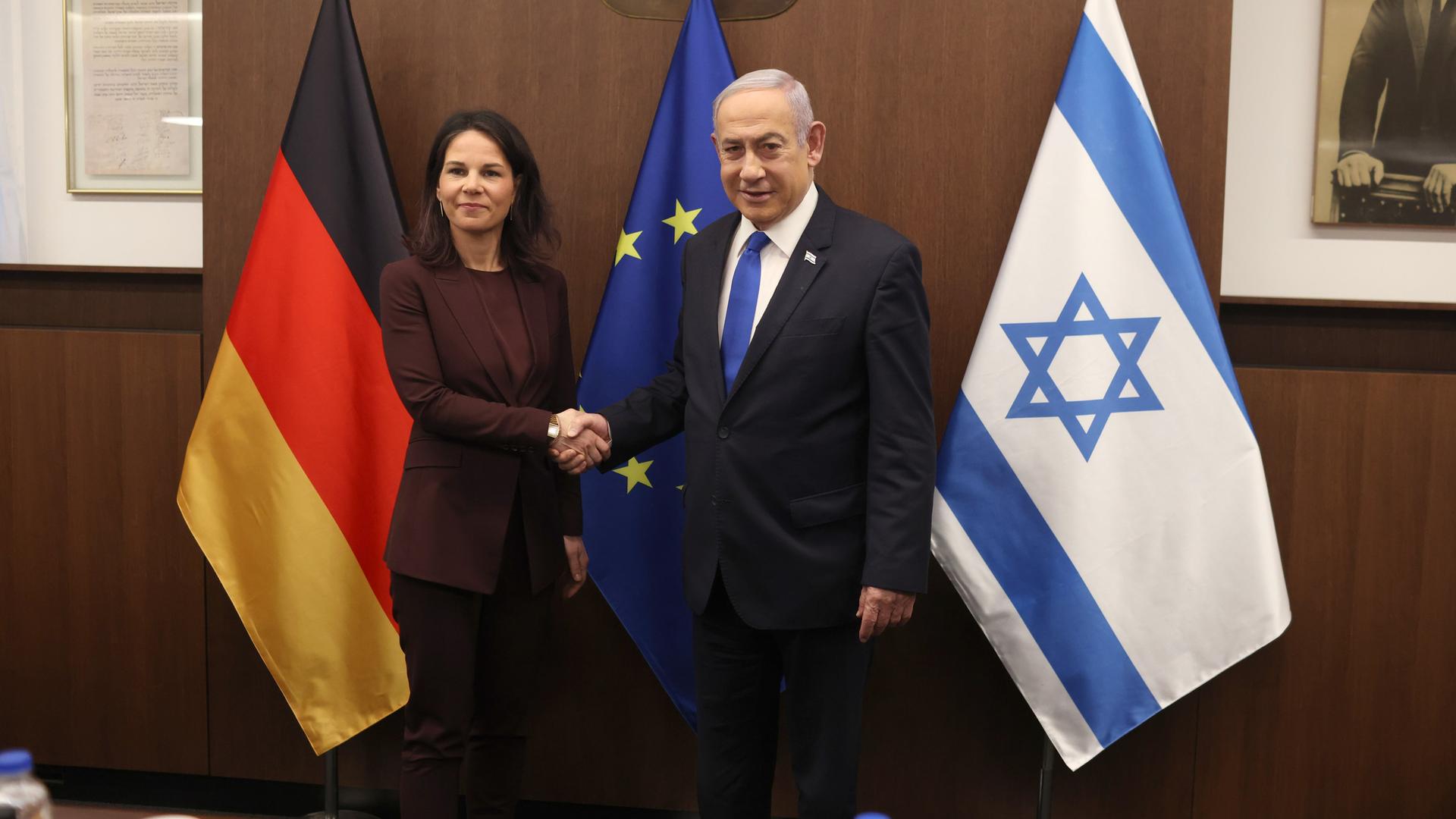 Bundesaußenministerin Baerbock (links) und Israels Ministerpräsident Netanjahu (rechts) stehen vor den Flaggen Deutschlands, der EU und Israels. Sie schütteln sich die Hände.