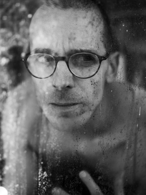 Ein Mann mt Brille und nacktem Oberkörper hinter eine Fensterscheibe Ein Mann mt Brille und nacktem Oberkörper hinter eine Fensterscheibe