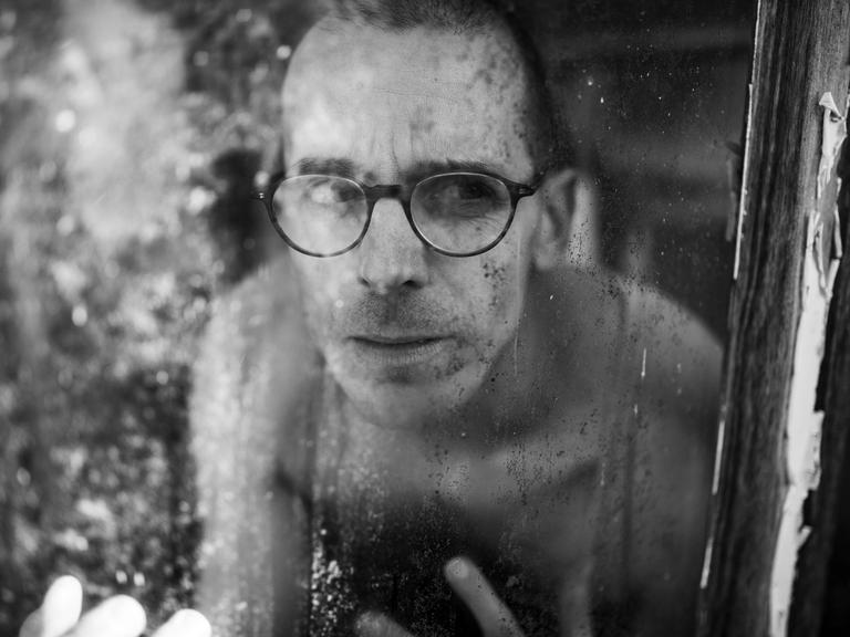 Ein Mann mt Brille und nacktem Oberkörper hinter eine Fensterscheibe Ein Mann mt Brille und nacktem Oberkörper hinter eine Fensterscheibe