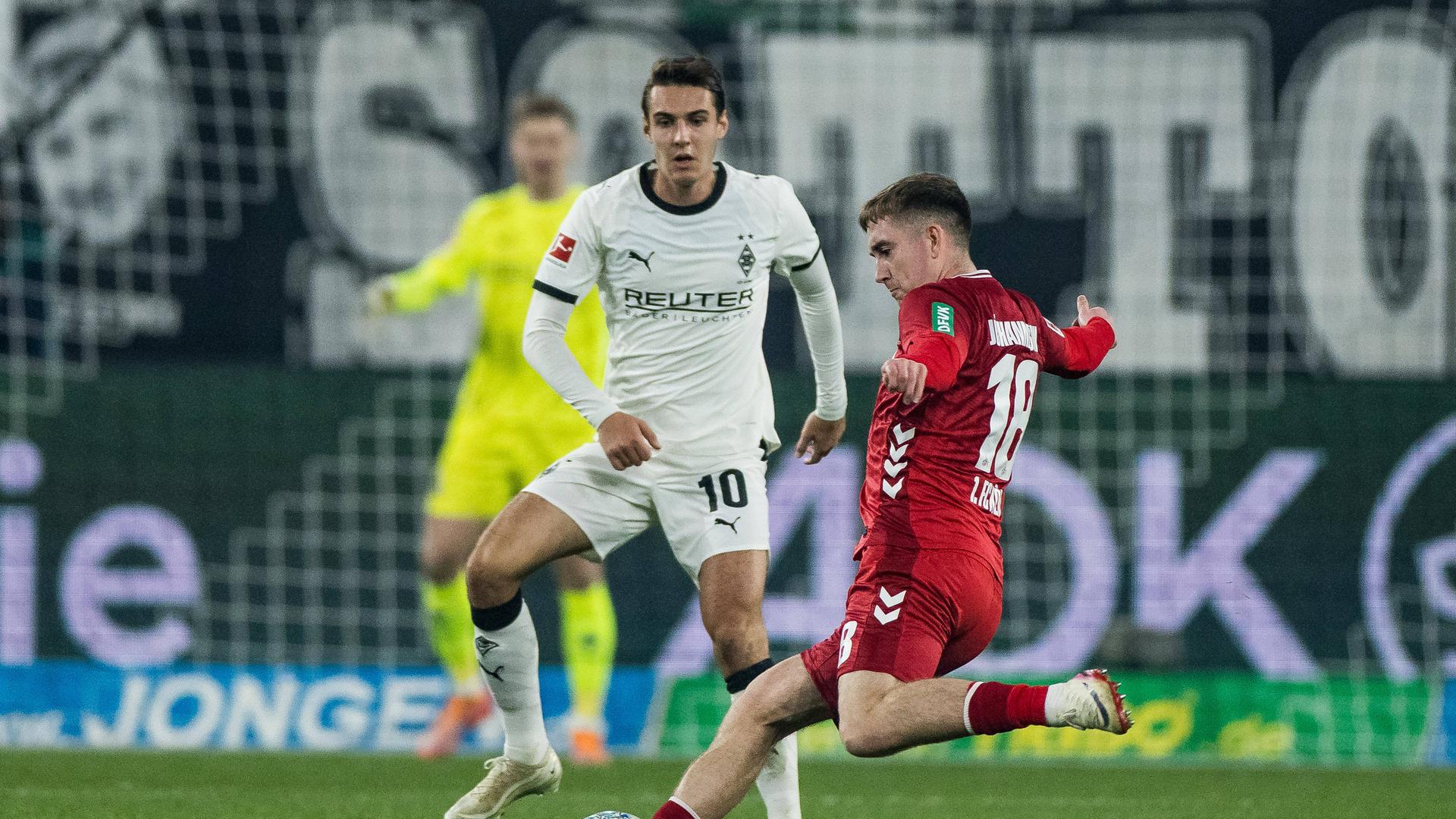 Zweikampf zwischen Florian Neuhaus von Borussia Mönchengladbach und Isak Johannesson vom 1. FC Köln. Johannesson tritt den Ball, während Neuhaus vor dem Tor steht.