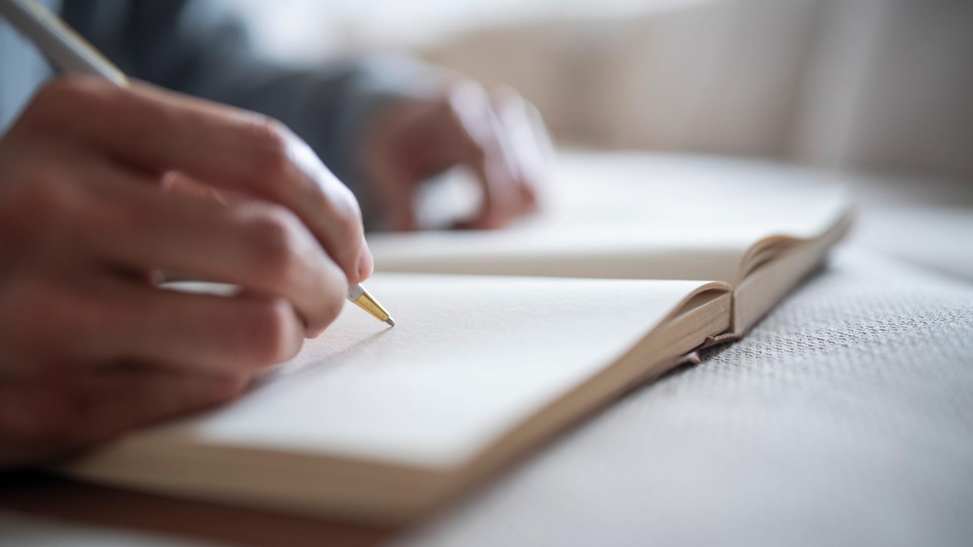 Nahaufnahme einer Hand mit einem Stift, die in ein Notizbuch schreibt.
